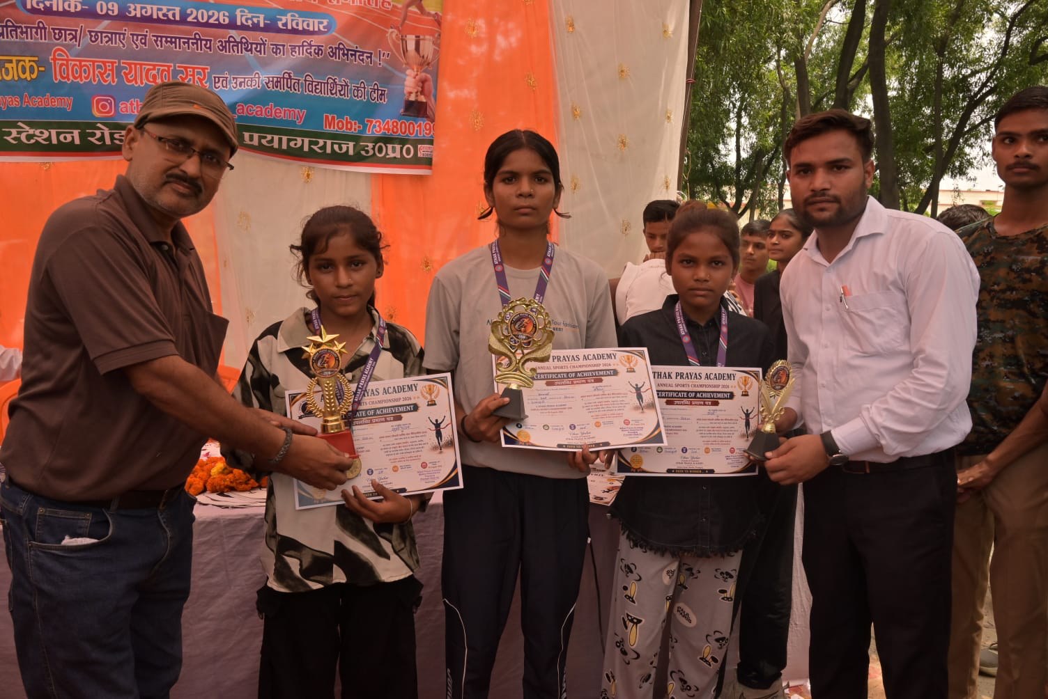 Students hold trophies and certificates at an outdoor sports awards ceremony
